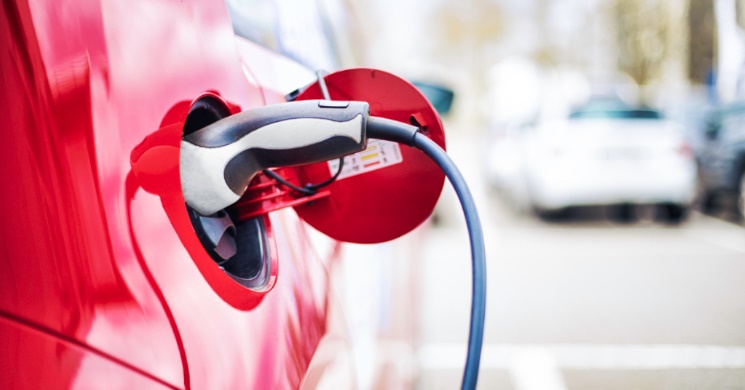 A red electric car is plugged in and charging